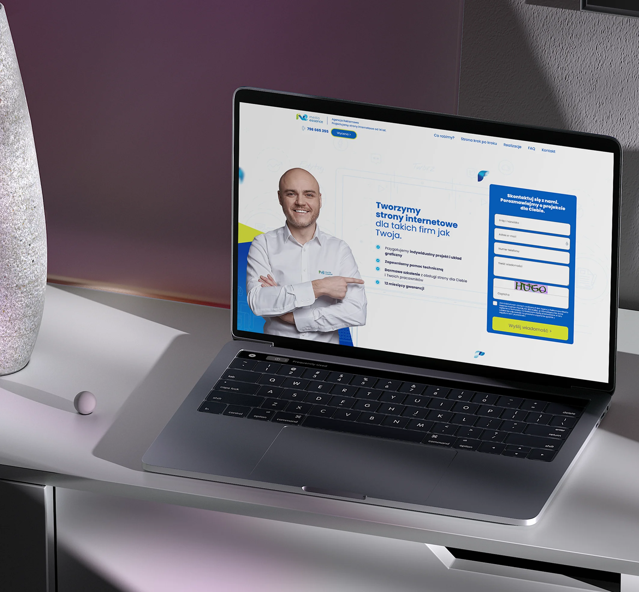 Obraz przedstawia laptopa ustawionego na biurku, na którego ekranie widnieje profesjonalna strona internetowa. Strona promuje usługi tworzenia stron internetowych dla firm, zawiera formularz kontaktowy oraz wizerunek uśmiechniętego specjalisty.