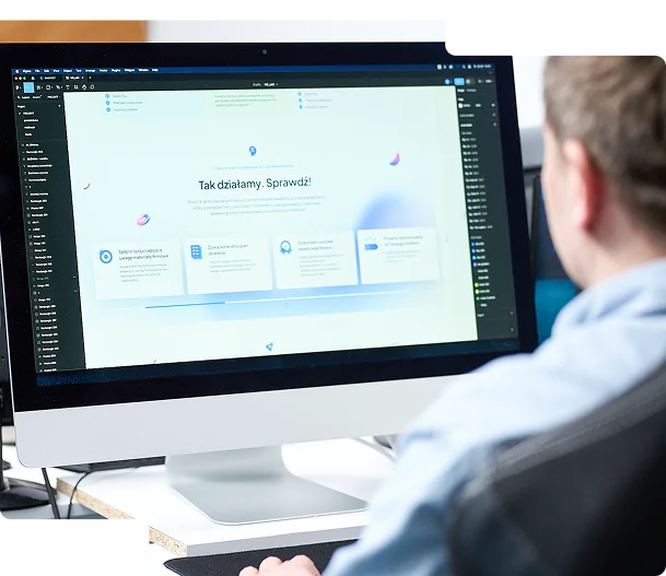 Na zdjęciu widać mężczyznę siedzącego przy biurku, pracującego na komputerze iMac. Na ekranie widnieje interfejs edytora graficznego lub narzędzia do projektowania stron internetowych