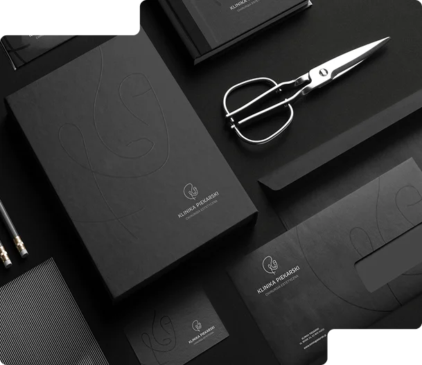 W skład zestawu wchodzą m.in. czarne foldery, koperty, wizytówki oraz akcesoria biurowe, takie jak nożyczki i ołówki. Widoczny na projektach logotyp „Klinika Piekarski” 